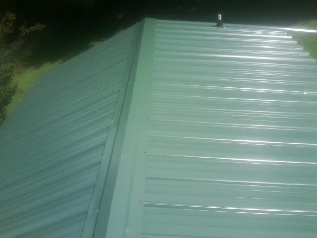 New green metal panels meeting at the ridge of a roof — Flat Roof Repair work by our crew in Allen
