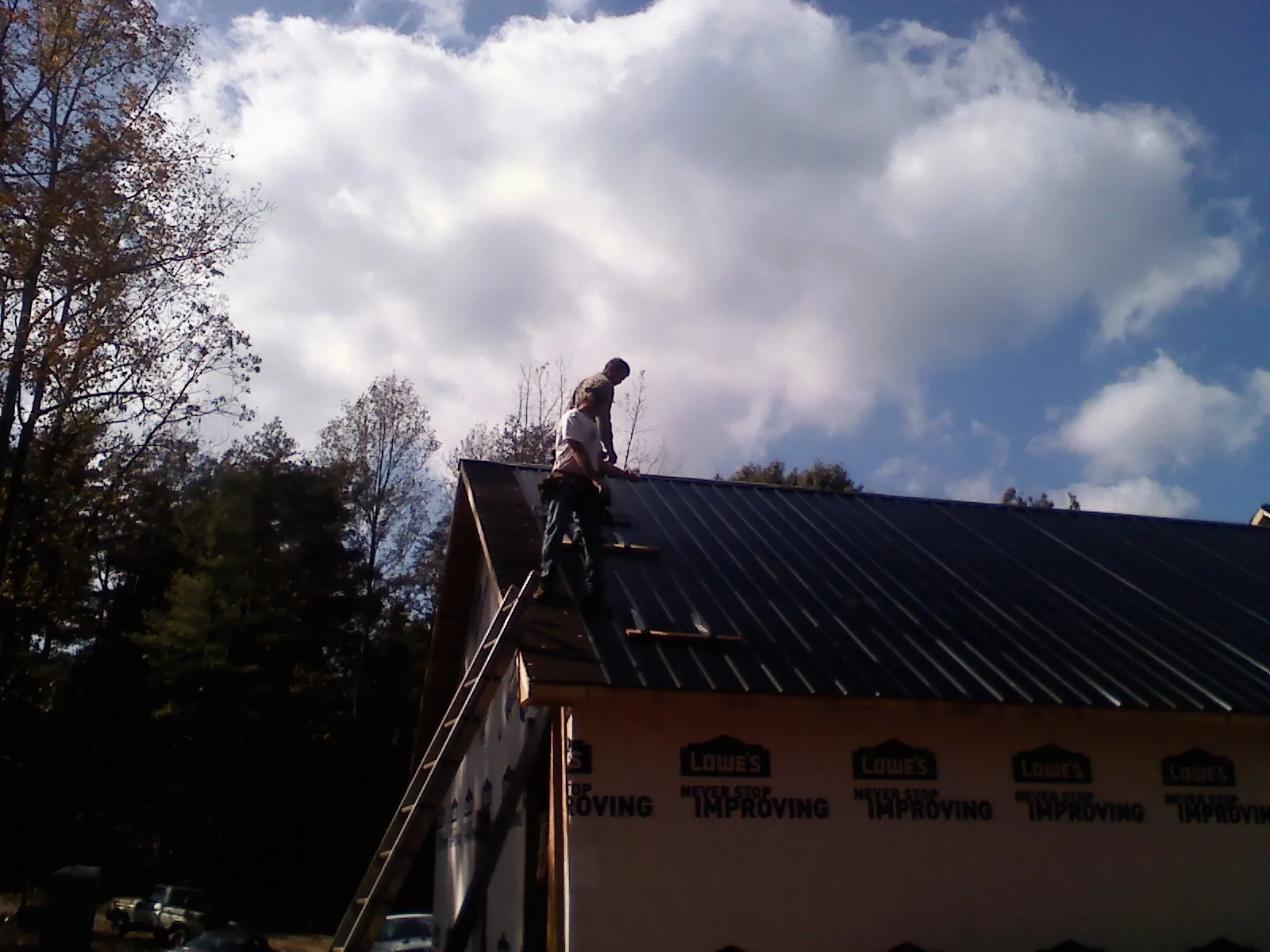 Roofer fastening dark metal panels high against a cloudy sky, from a Roof Inspection job in Allen